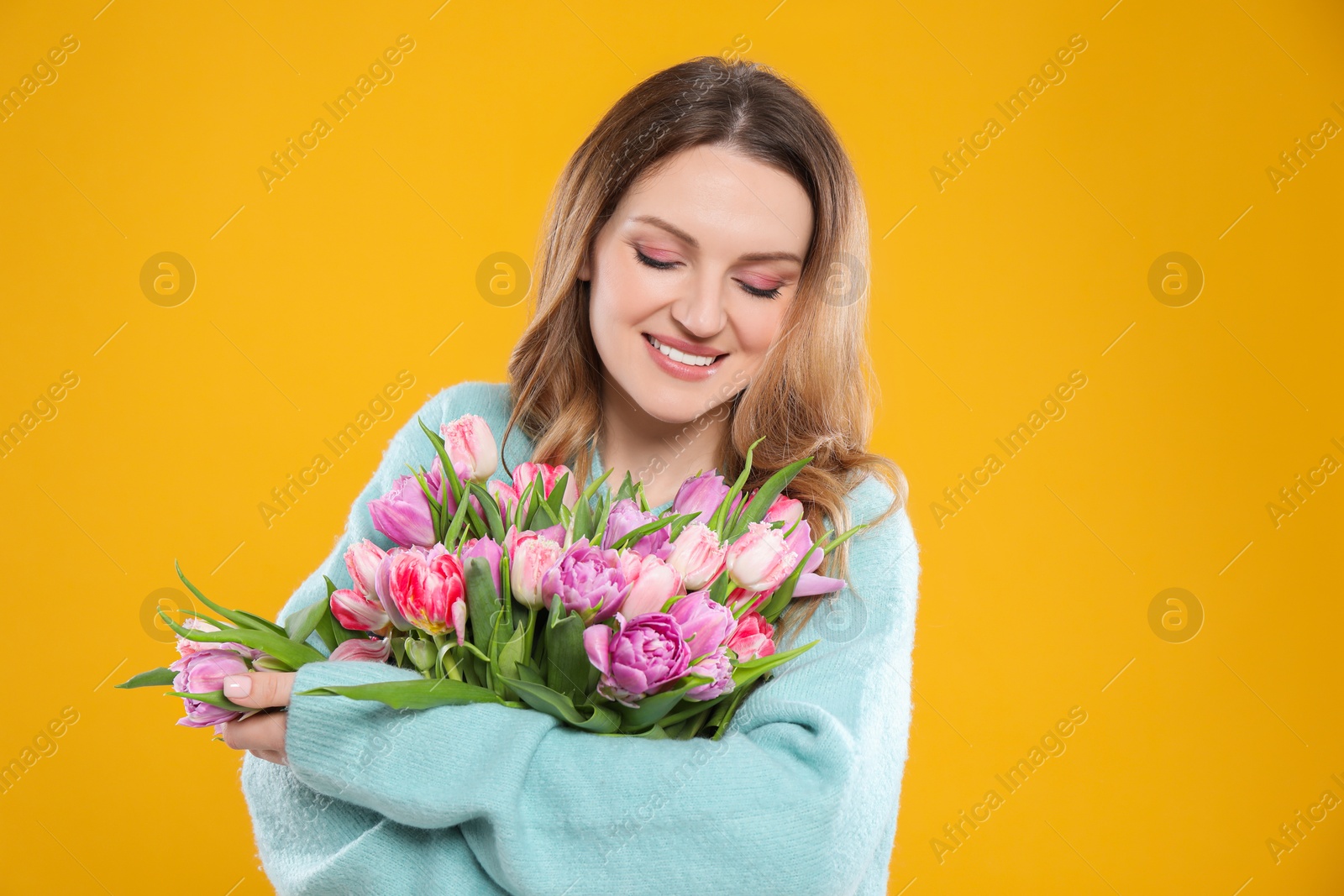 Photo of Happy young woman with bouquet of beautiful tulips on yellow background