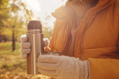 Photo of Woman with metallic thermos and cap outdoors, closeup