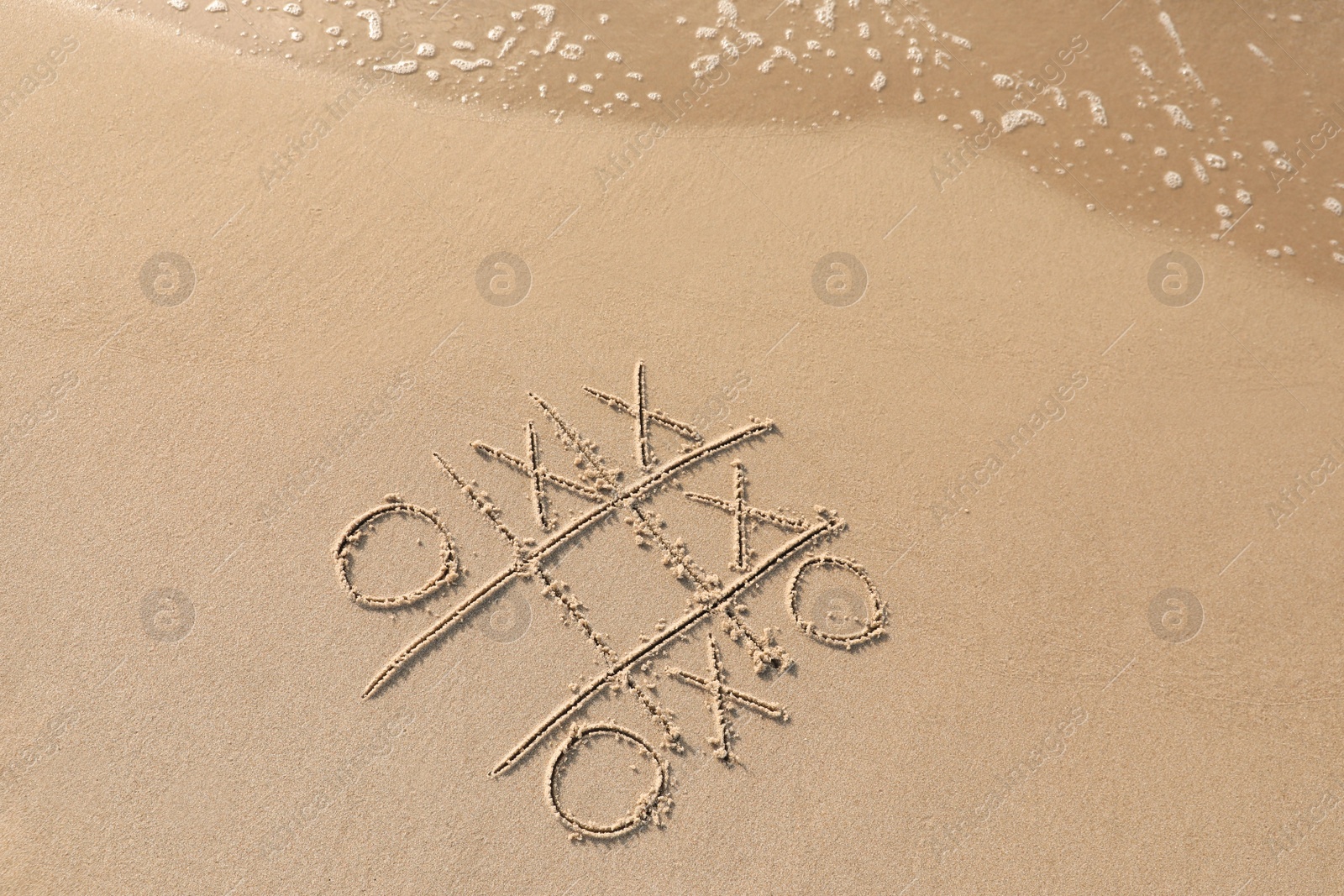 Photo of Tic tac toe game drawn on sand near sea, top view. Space for text