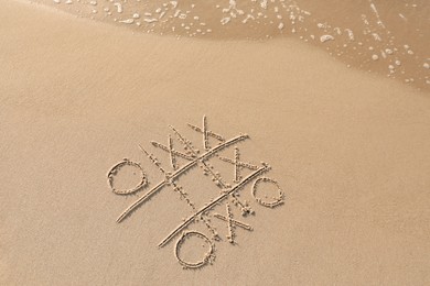 Tic tac toe game drawn on sand near sea, top view. Space for text