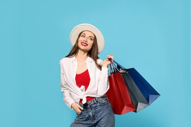 Photo of Stylish young woman with shopping bags on light blue background