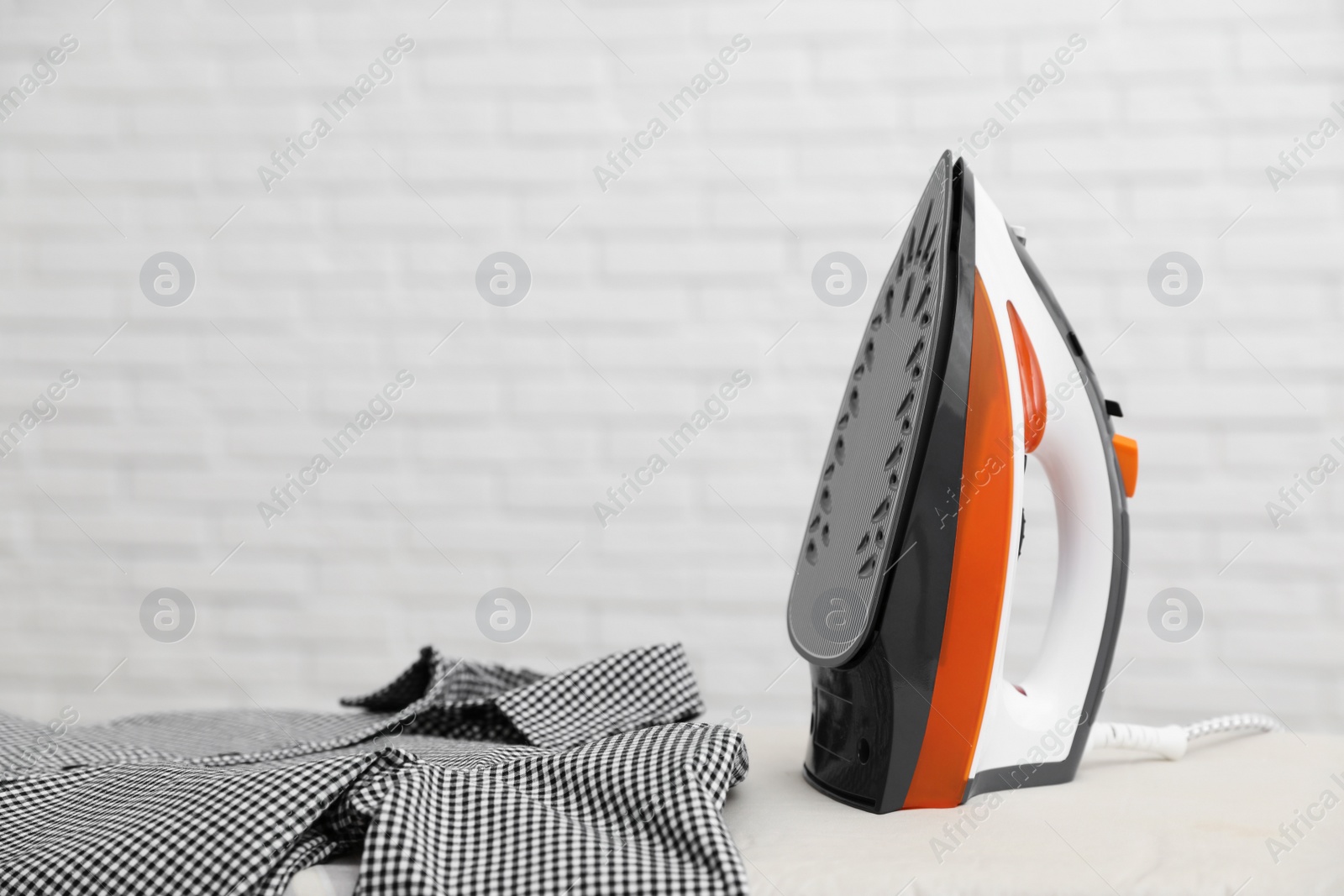 Photo of New modern iron and clean shirt on board against light background, space for text. Laundry day