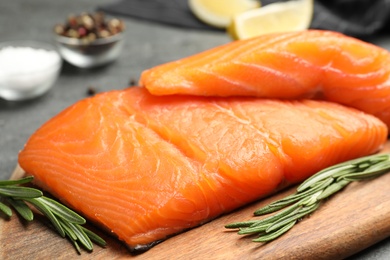 Photo of Wooden board with salmon fillet on grey table, closeup