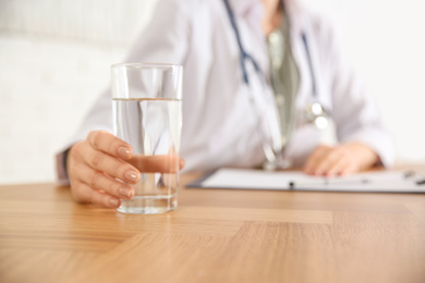 Photo of Nutritionist with glass of water at desk in office, closeup