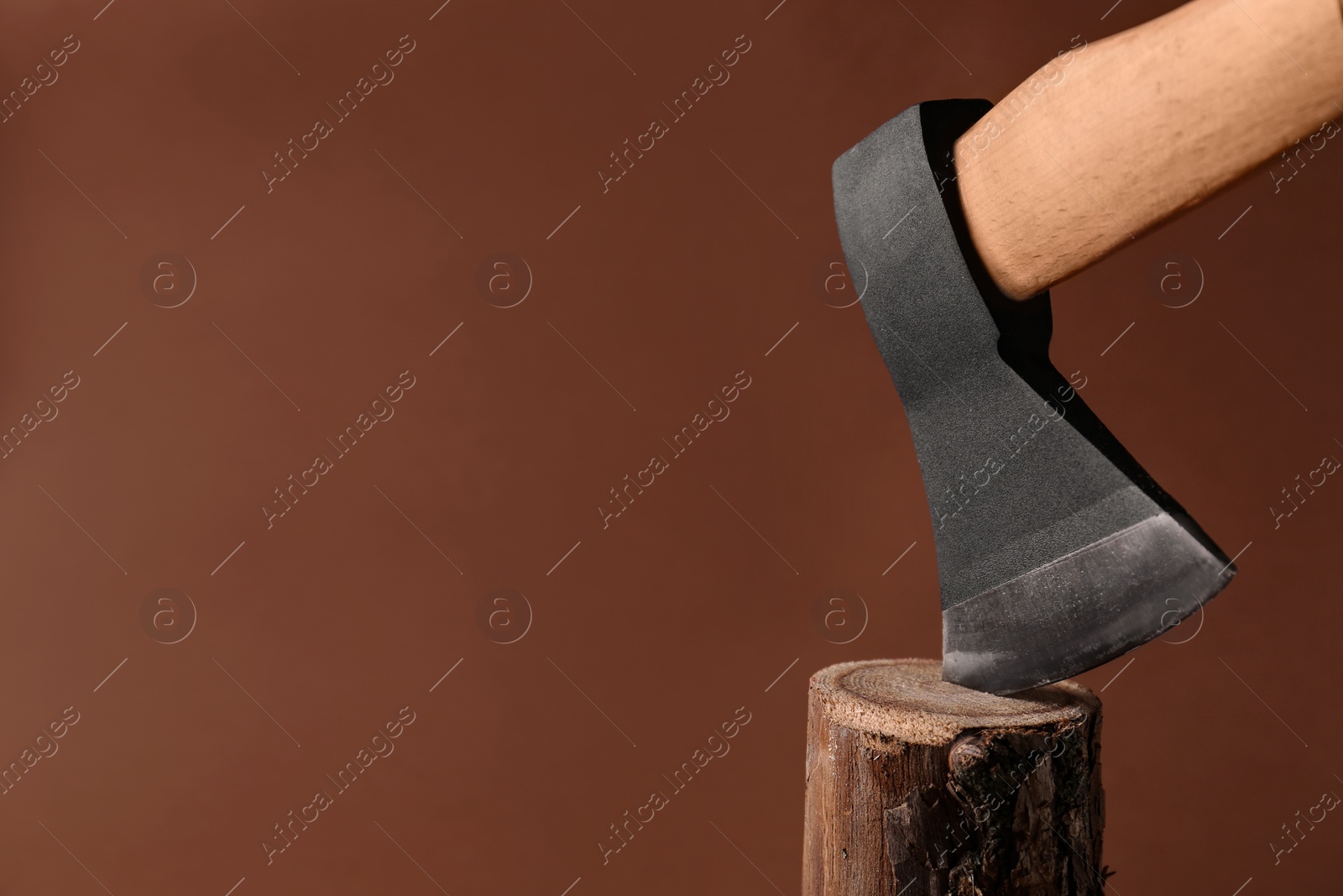 Photo of Metal ax in wooden log on brown background. Space for text