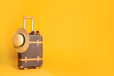 Photo of Vintage travel suitcase with hat and sunglasses on yellow background, space for text. Summer vacation