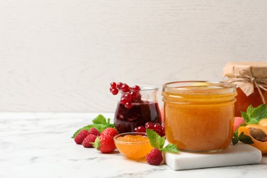 Photo of Jars with different jams and fresh fruits on white marble table. Space for text