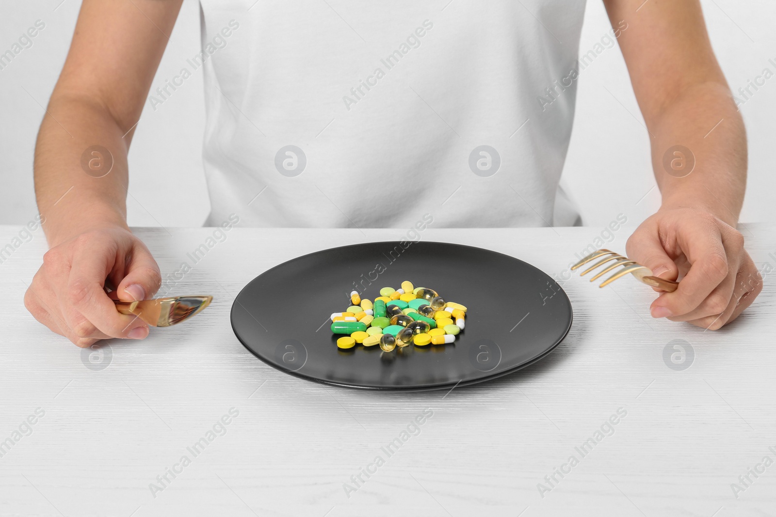 Photo of Woman sitting at table with cutlery and plate of weight loss pills, closeup