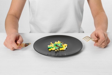 Woman sitting at table with cutlery and plate of weight loss pills, closeup