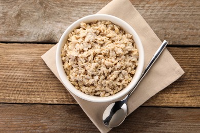 Photo of Tasty boiled oatmeal in bowl and spoon on wooden table, top view