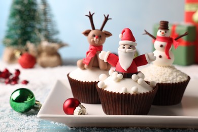 Photo of Different beautiful Christmas cupcakes on blue table with festive decor and snow