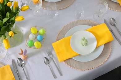 Photo of Festive table setting with glasses, painted eggs and vase of tulips. Easter celebration