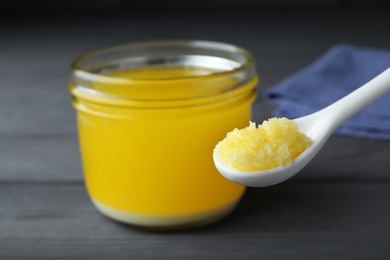 Photo of Glass jar and spoon of Ghee butter on grey wooden table, closeup