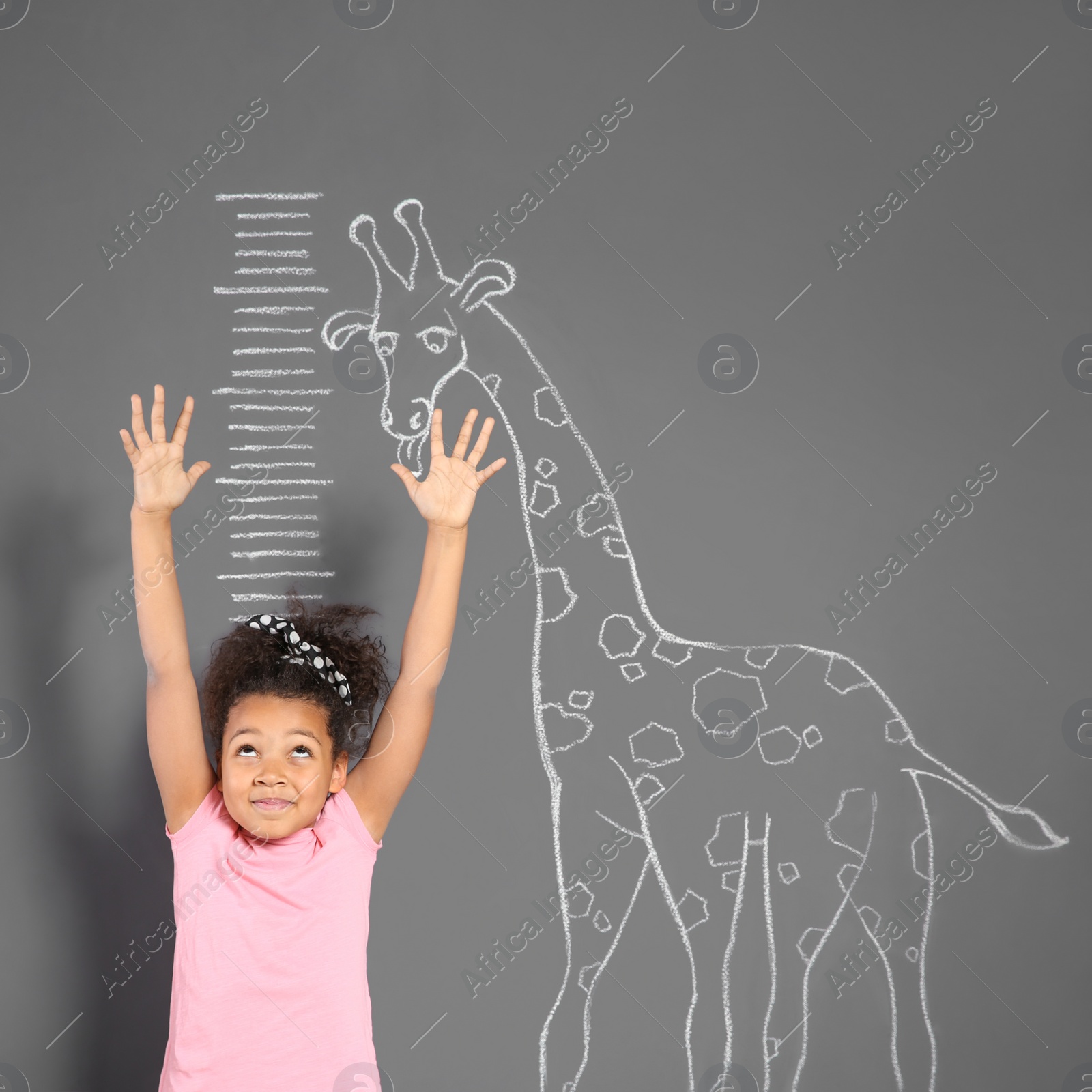 Photo of African-American child measuring height near chalk giraffe drawing on grey wall