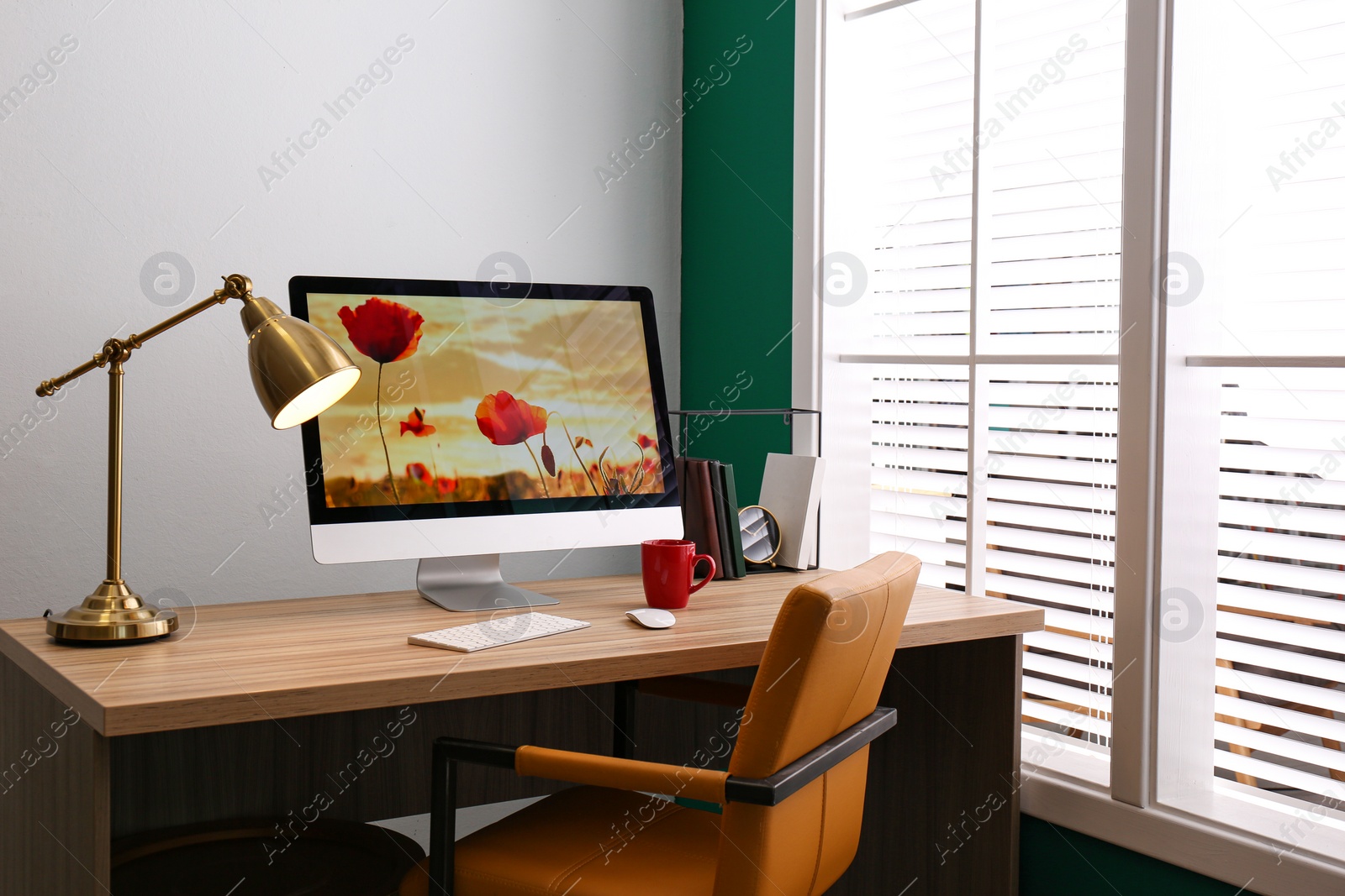 Photo of Comfortable workplace near window with white horizontal blinds in room