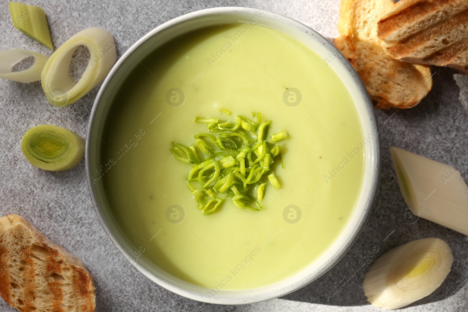 Photo of Bowl of delicious soup, cut leek and croutons on grey table, flat lay