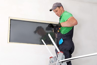 Photo of Worker in uniform installing double glazing window indoors