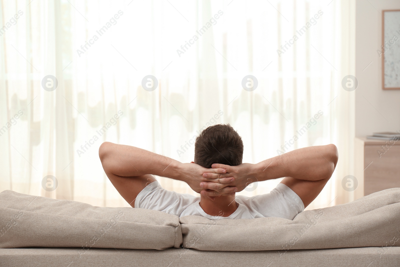 Photo of Man relaxing on sofa at home, back view