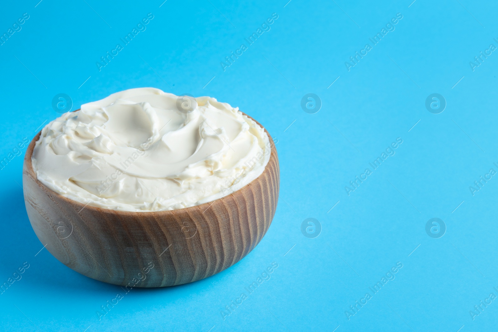 Photo of Bowl of tasty cream cheese on light blue background, space for text