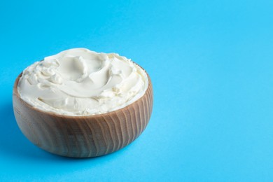 Photo of Bowl of tasty cream cheese on light blue background, space for text