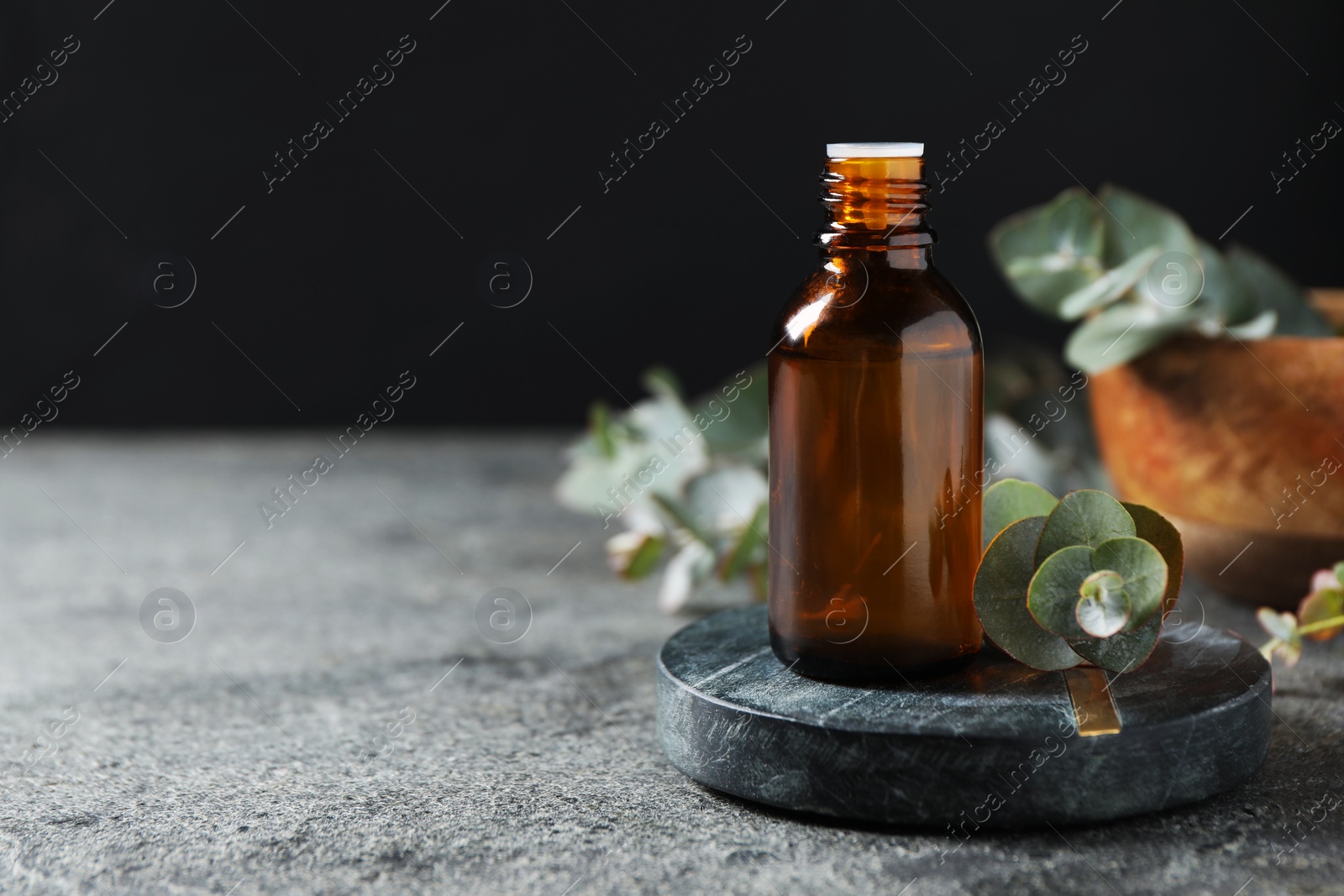 Photo of Bottle of eucalyptus essential oil and plant branches on grey table, space for text