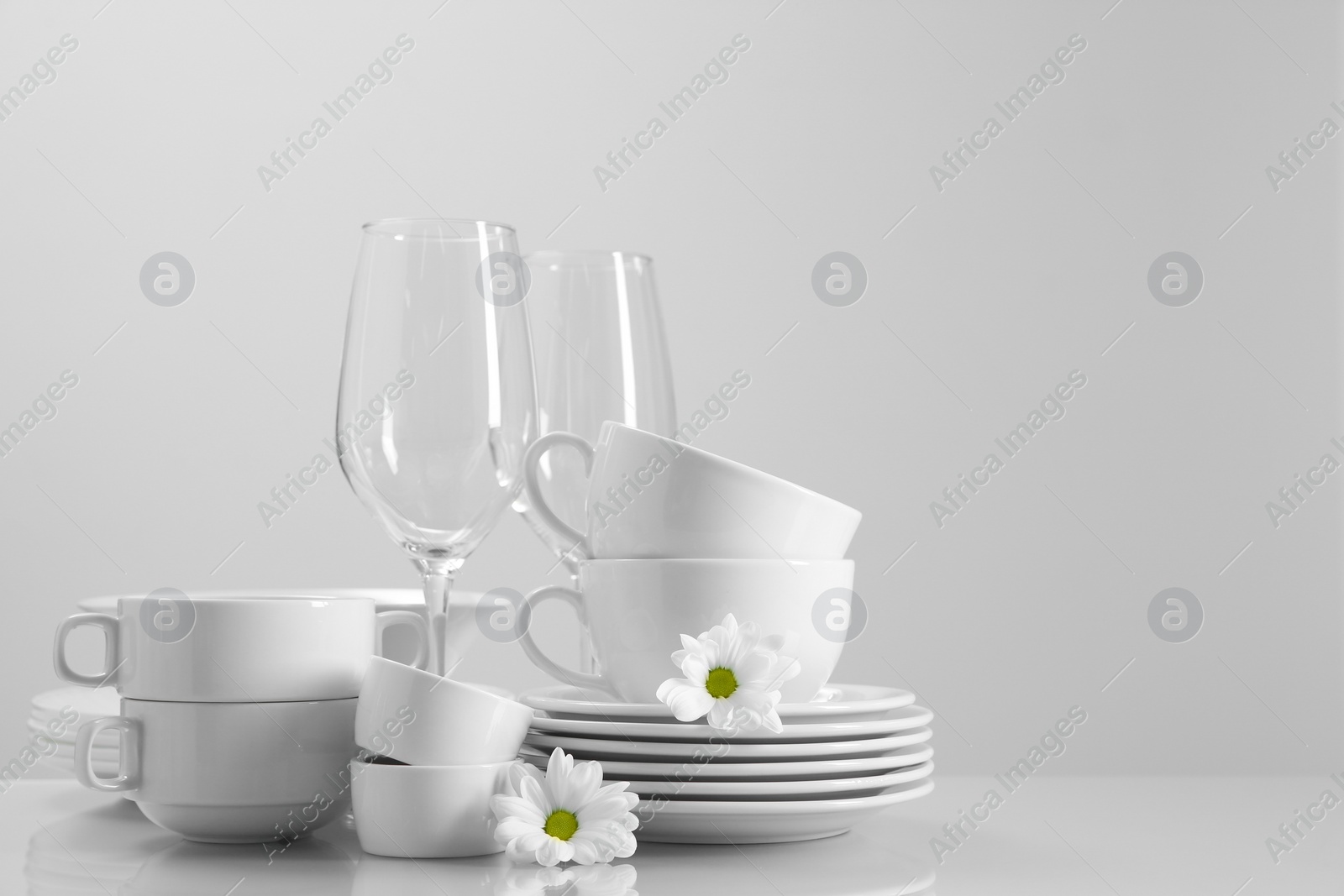 Photo of Set of many clean dishware, flowers and glasses on light table. Space for text