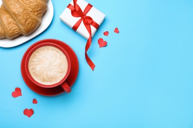 Photo of Cup of coffee, croissant and gift box on turquoise background, flat lay with space for text. Valentine's day breakfast