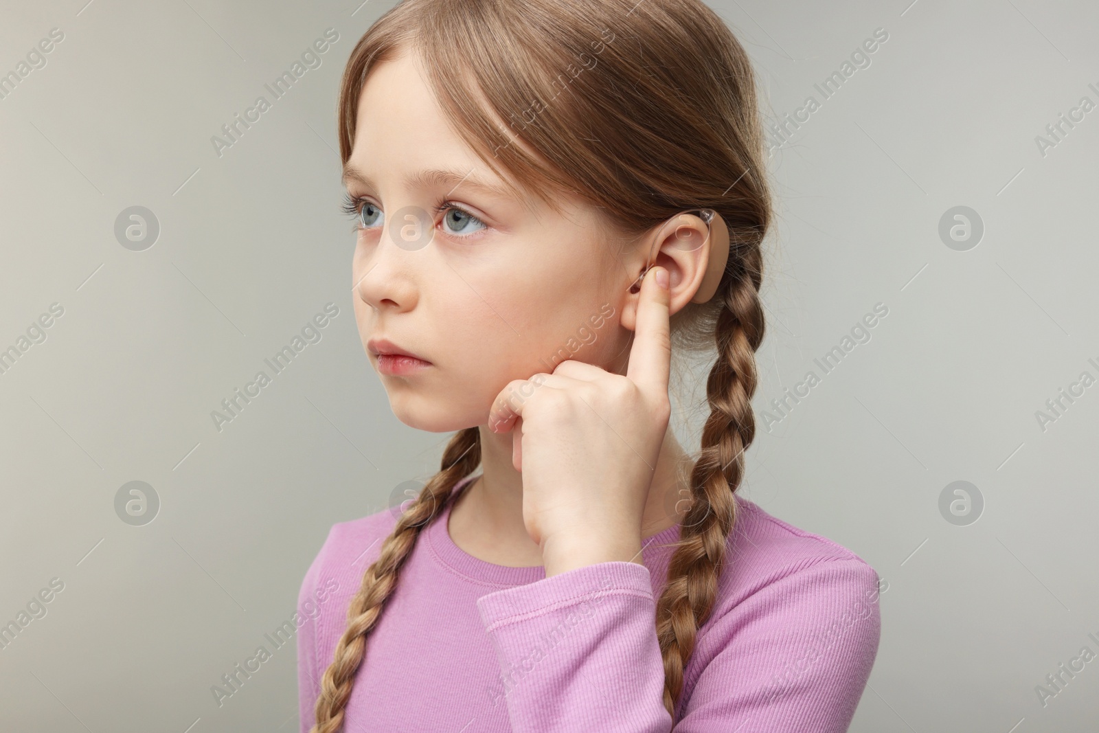 Photo of Little girl with hearing aid on grey background