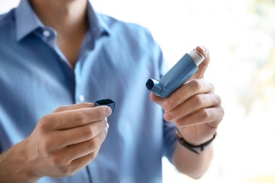 Photo of Young man with asthma inhaler indoors, closeup