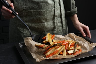 Cooker near baking pan with tasty parsnip and bell pepper at dark grey table, closeup