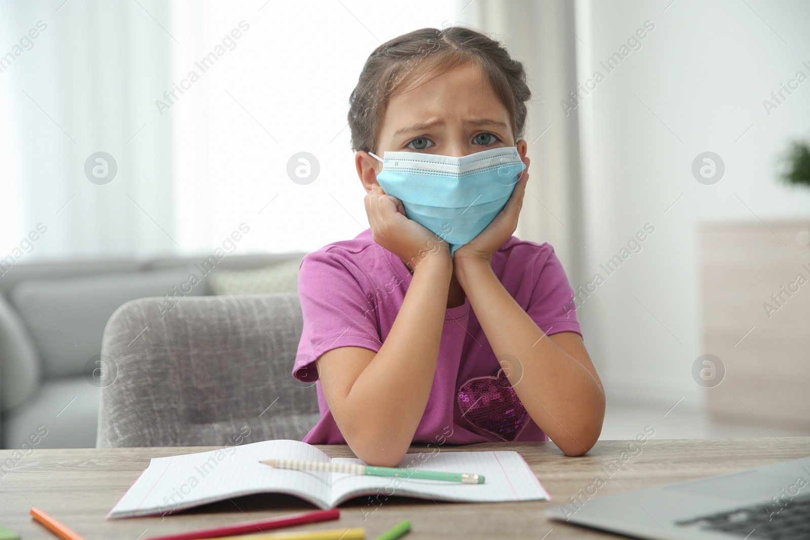 Photo of Distance learning, online studying at home due to Covid-19 pandemic. Girl in protective mask doing homework in room