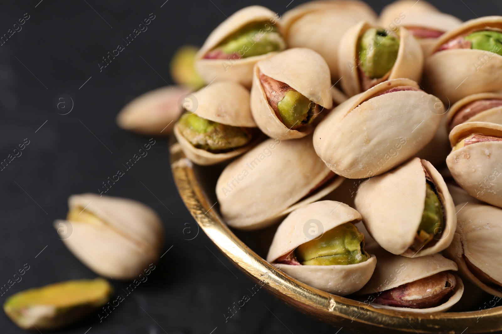 Photo of Tasty pistachios in bowl on black table, closeup