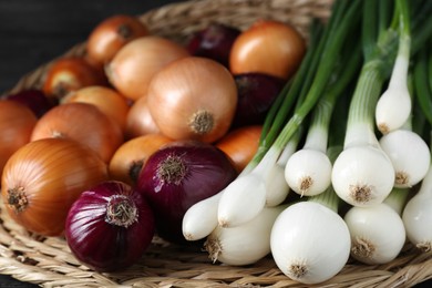 Different kinds of onions on wicker mat, closeup