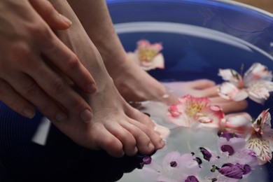 Photo of Woman soaking her feet in bowl with water and flowers, closeup. Spa treatment