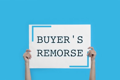 Image of Woman holding poster with text Buyer's Remorse on light blue background, closeup