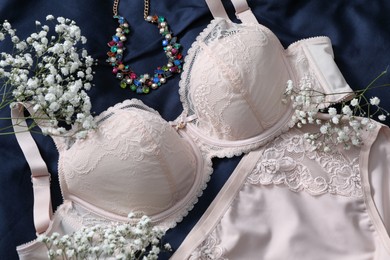 Photo of Elegant plus size women's underwear, gypsophila flowers and necklace on dark blue fabric, closeup