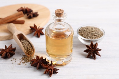 Bottle of essential oil, anise and seeds on white wooden table