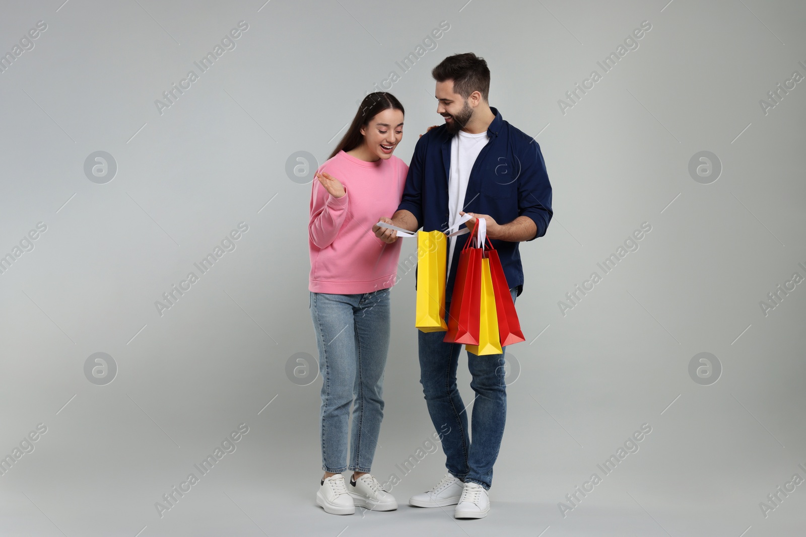 Photo of Man showing to his girlfriend shopping bag with purchase on grey background