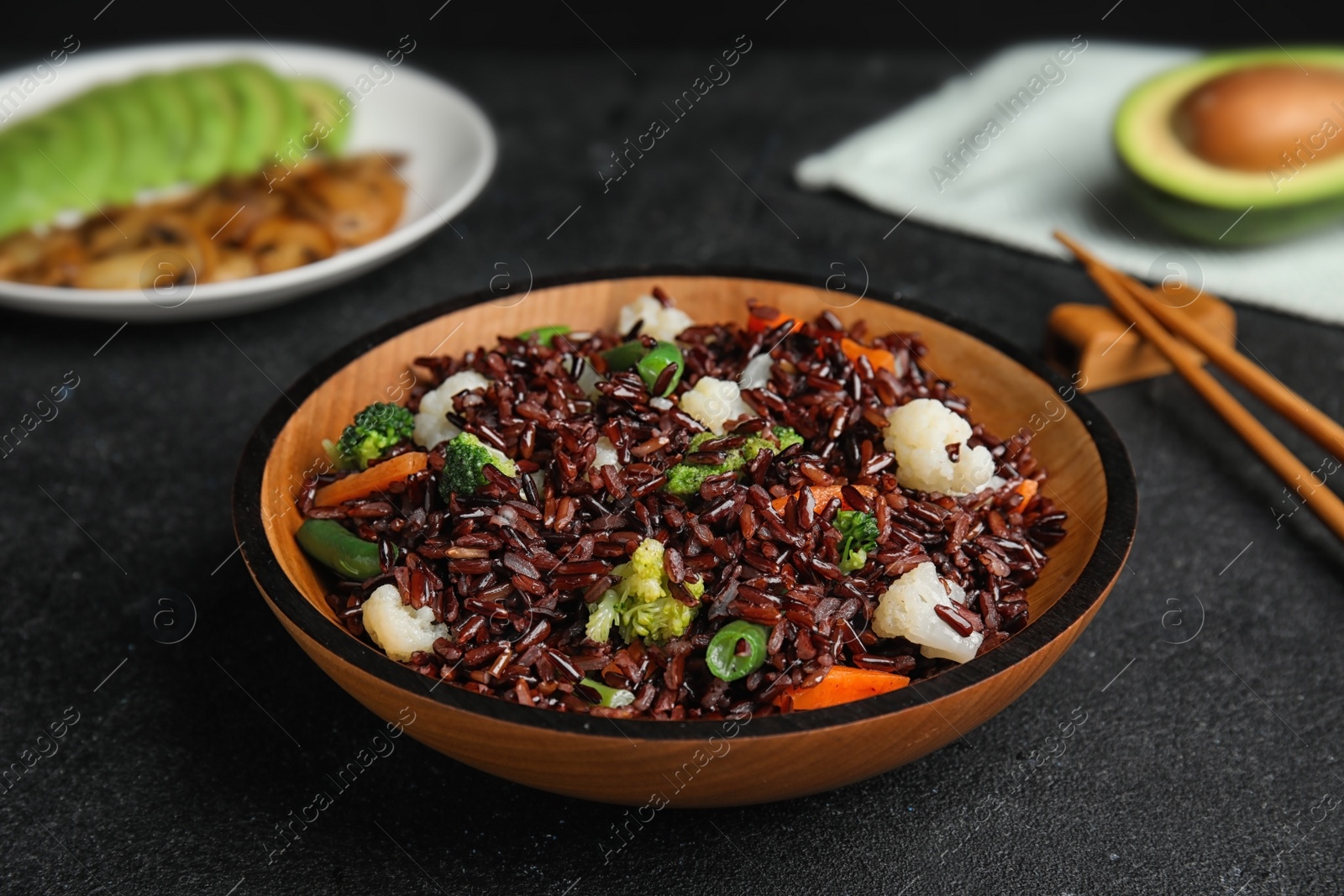 Photo of Plate of brown rice with vegetables on black table