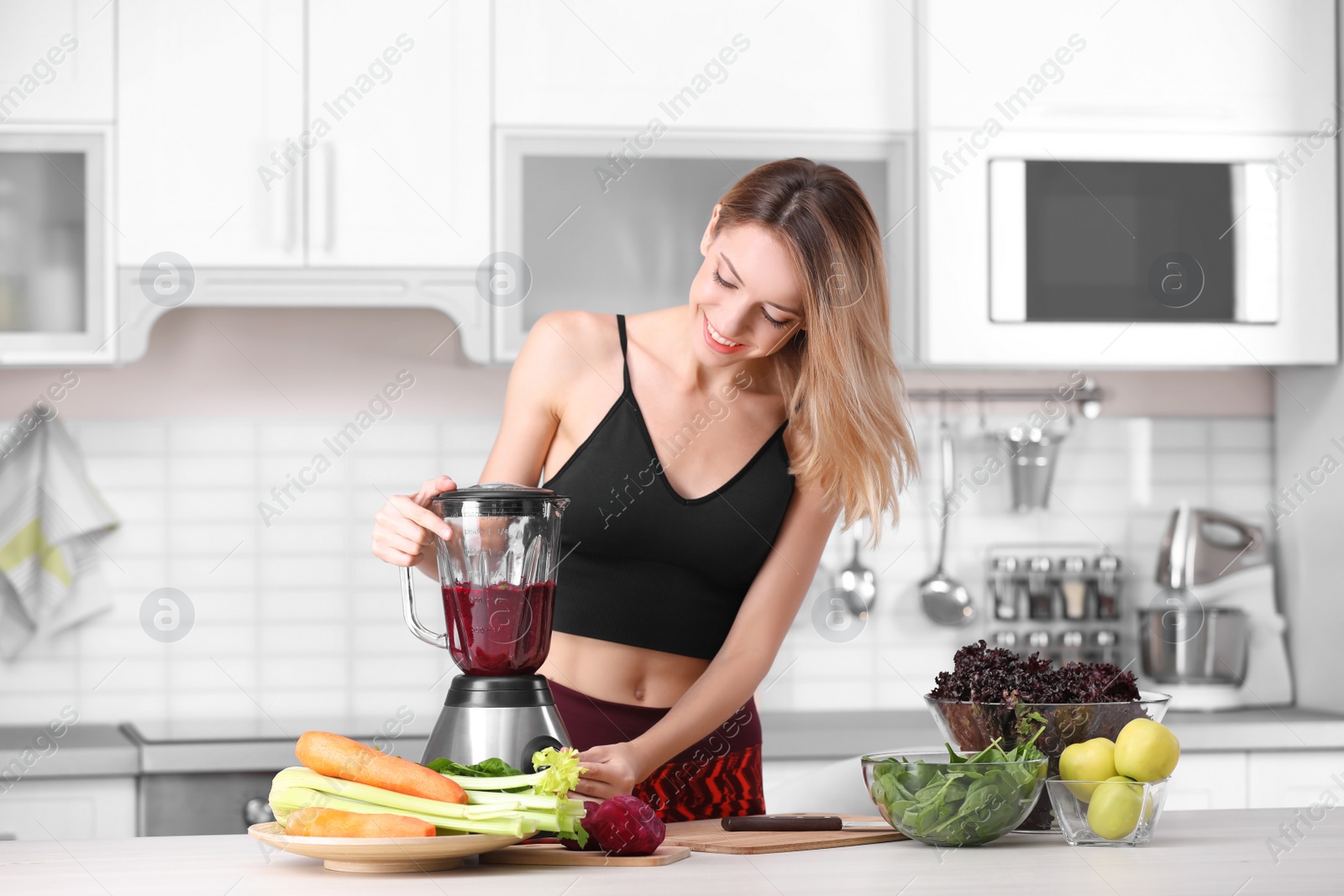 Photo of Young woman preparing tasty healthy smoothie at table in kitchen