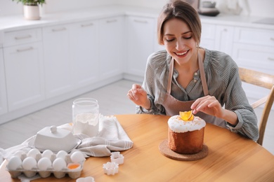 Young woman decorating traditional Easter cake in kitchen. Space for text