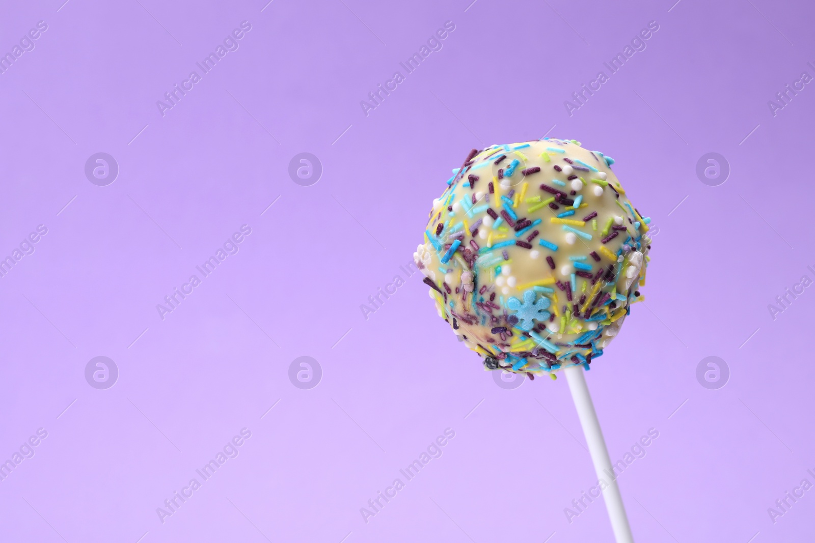 Photo of Delicious confectionery. Sweet cake pop decorated with sprinkles on light violet background, closeup. Space for text