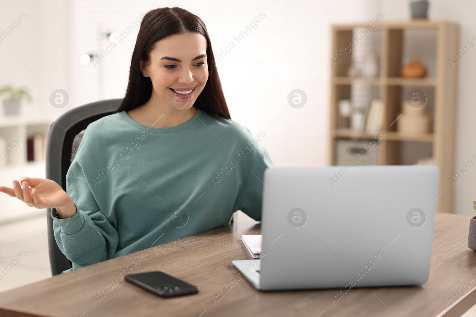 Photo of Young woman using video chat during webinar at table in room