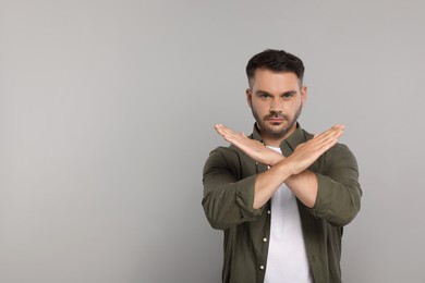 Photo of Handsome man with crossed hands on light grey background, space for text. Stop gesture