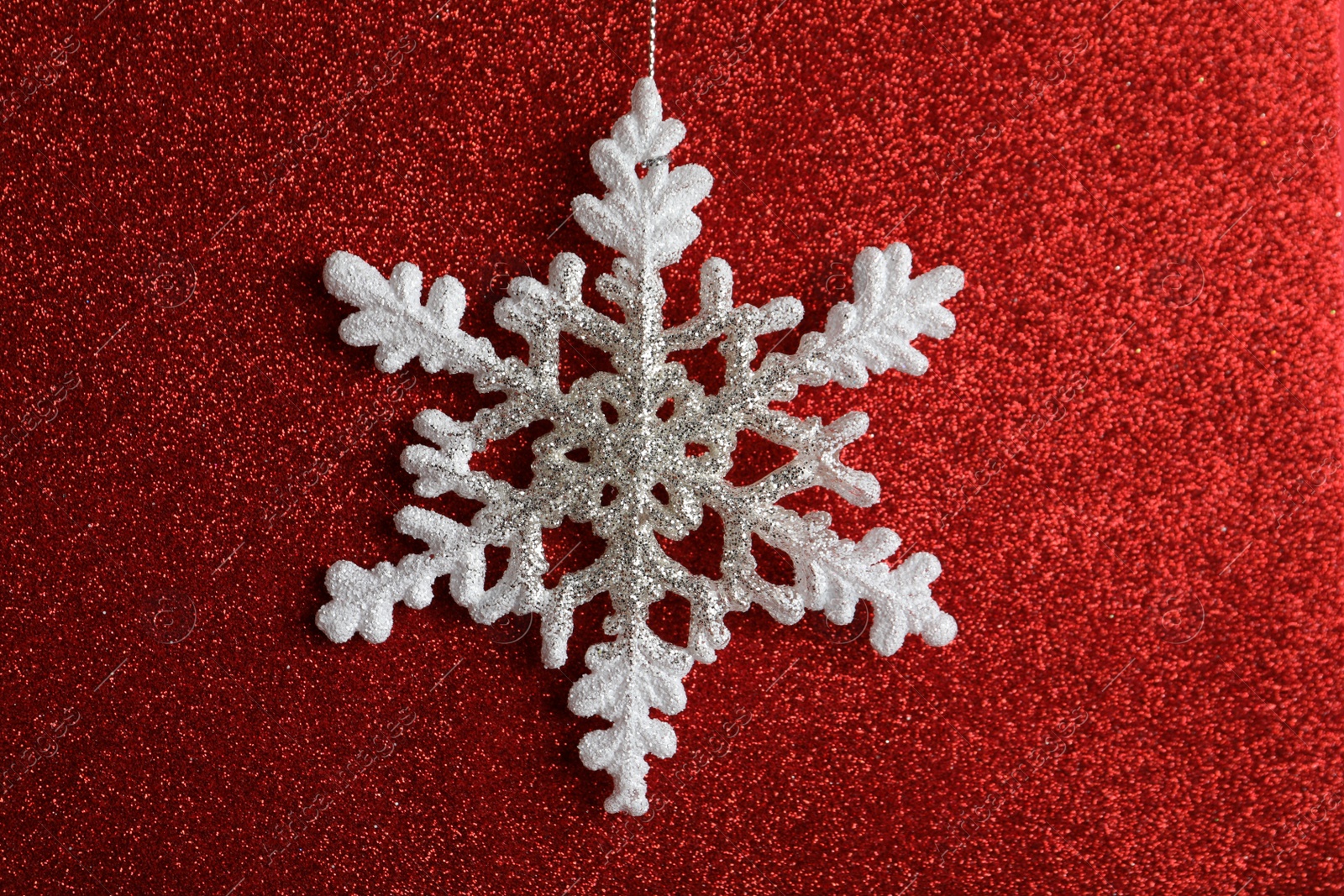 Photo of Beautiful decorative snowflake hanging on sparkling red glitter background, closeup