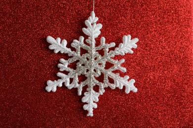 Photo of Beautiful decorative snowflake hanging on sparkling red glitter background, closeup
