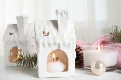 Composition with candles in house shaped holders on white wooden table. Christmas decoration