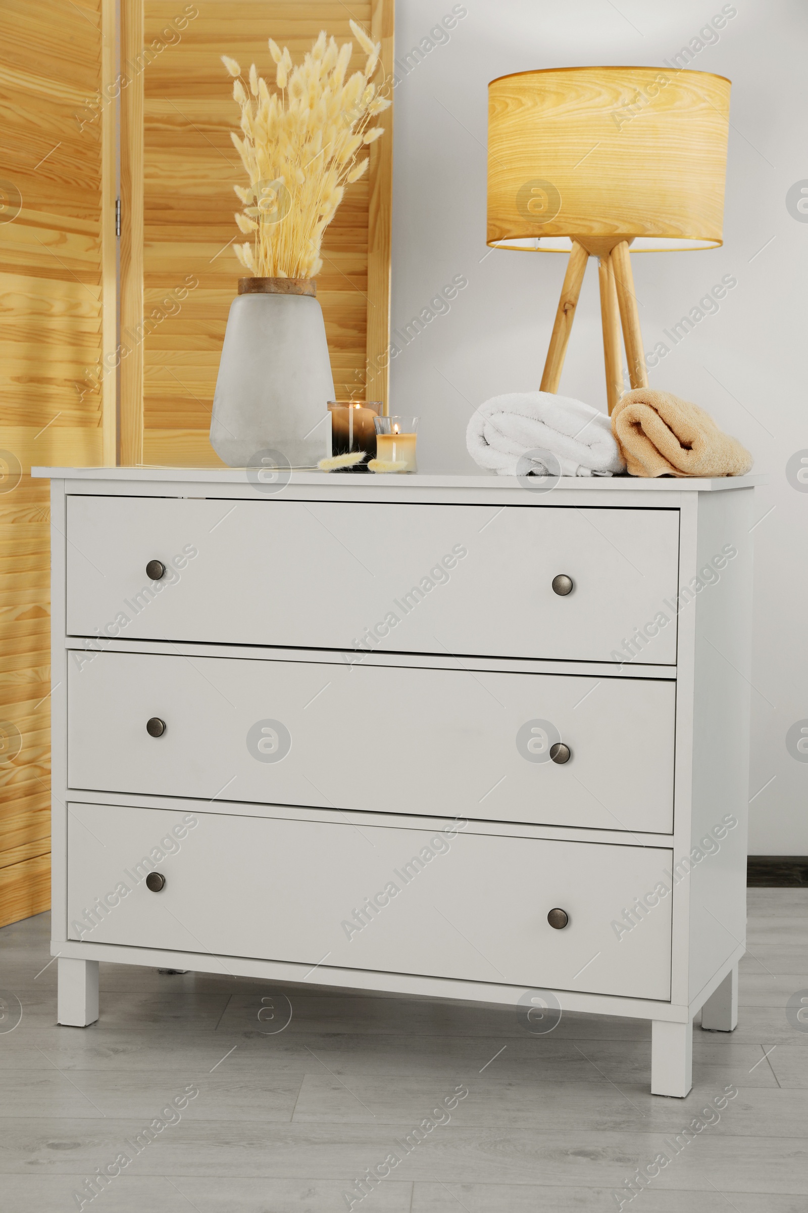 Photo of Vase with dried flowers, stacked towels and candles on chest of drawers in room. Interior design