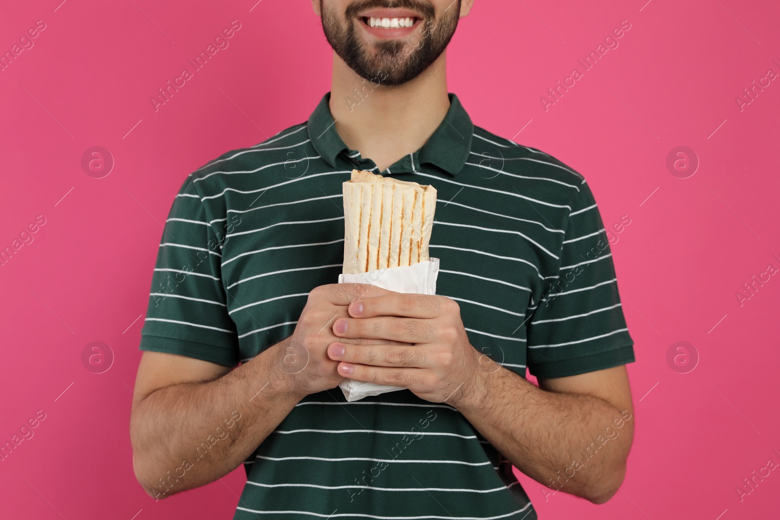 Photo of Happy young man holding tasty shawarma on pink background, closeup