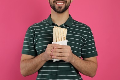 Photo of Happy young man holding tasty shawarma on pink background, closeup